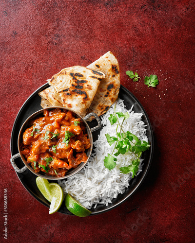 Chicken tikka masala spicy curry meat food Butter chicken, rice and naan bread on red vine dark background. Traditional Indian dish, top view, close up, copy space. photo