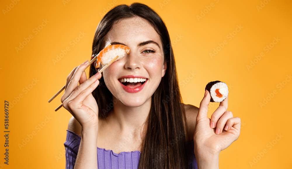 Happy woman with asian food. Girl with chopsticks eats sushi rolls and nigiri, order take out delivery, orange background Happy woman with asian food. Girl with chopsticks eats sushi rolls and nigiri, order take out delivery, orange background