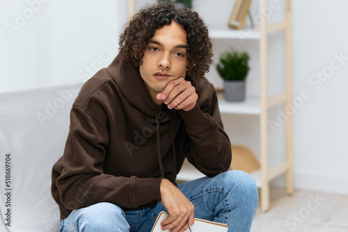 guy with curly hair sit on a chair with a notepad and a writing pen isolated background