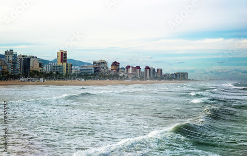 beautiful view of the beach of the coastal city from the side of the rough sea with mountains on a background