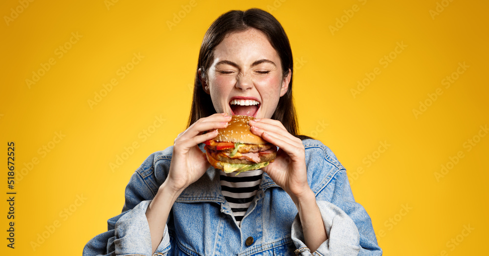 Girl bites cheeseburger with pleasure. Woman eating hambuger, order burger for takeaway food delivery at fastfood restaurant - obrazy, fototapety, plakaty 