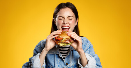Girl bites cheeseburger with pleasure. Woman eating hambuger, order burger for takeaway food delivery at fastfood restaurant