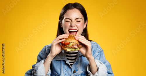 Girl bites cheeseburger with pleasure. Woman eating hambuger, order burger for takeaway food delivery at fastfood restaurant photo