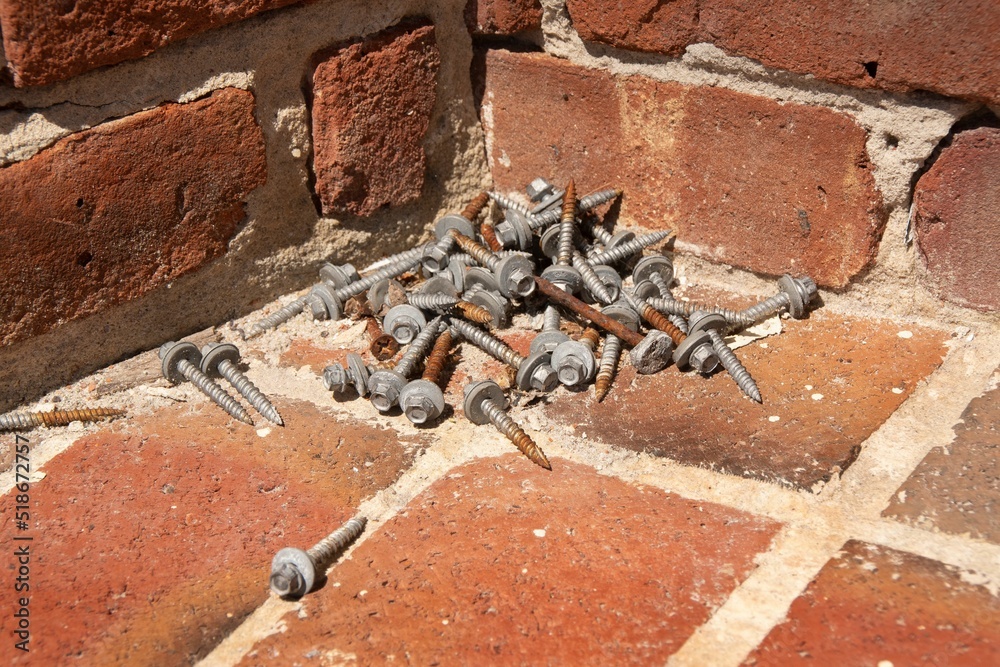 Pile of bolts and nuts laying on a corner of a brick floor outside of a