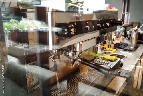 A Picture of a Coffee Making Machine Inside a Coffee Shop Taken from Outside the Window with Some Reflection of Outside Scene