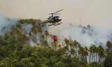 Un elicottero sta portando un bucket con acqua per spengere il fuoco nel bosco