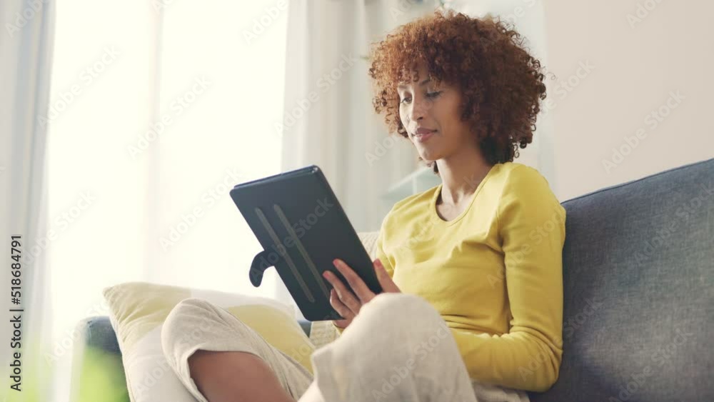 One young female freelancer smiling while browsing blogs, scrolling social media and streaming series online to enjoy on the weekend. Happy woman using a digital tablet on a sofa at home. One young female freelancer smiling while browsing blogs, scrolling social media and streaming series online to enjoy on the weekend. Happy woman using a digital tablet on a sofa at home.