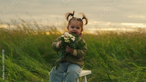 Funny girl sits on a chair with flowers in her hands. Outdoors.