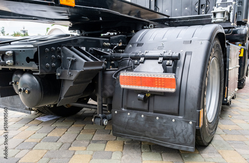 Detail of the rear of a new utility truck. Taillights, electrical connectors, plastic mudguards, wheels and rims. Red brake lights and orange turn signals. Road safety