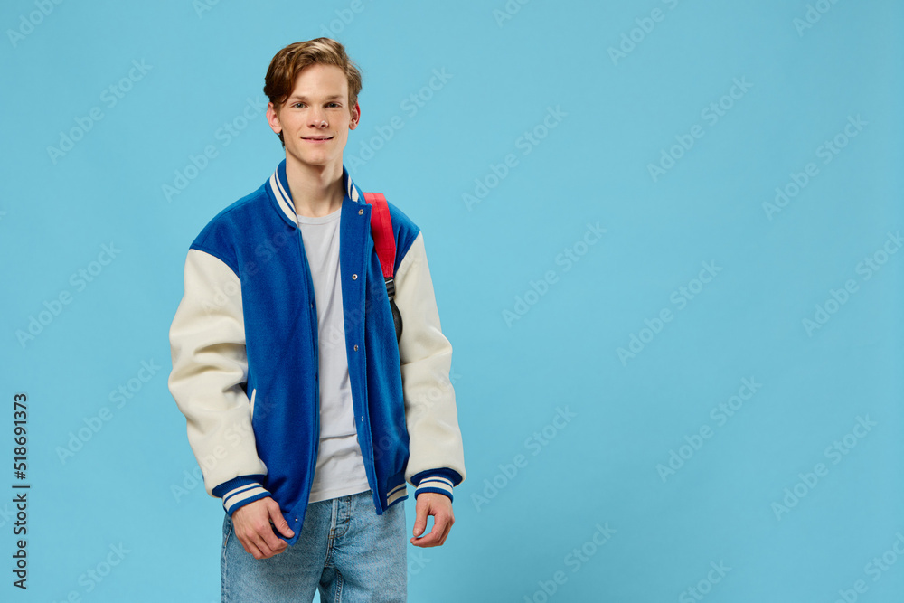 horizontal portrait of a handsome, joyful student guy with a red backpack on his shoulder, looking at the camera