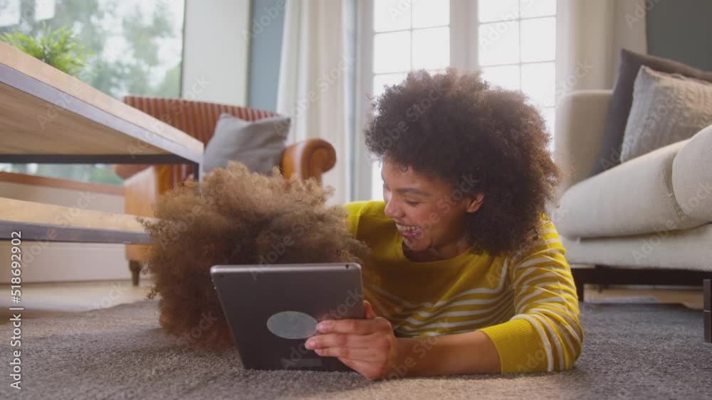 Mother and daughter having fun lying on floor streaming movie on digital tablet at home together - shot in slow motion