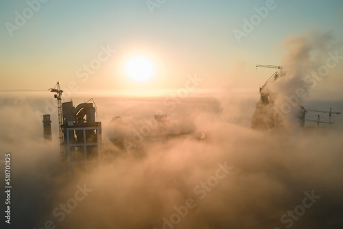 Aerial view of cement factory with high concrete plant structure and tower crane at industrial production site on foggy morning. Manufacture and global industry concept