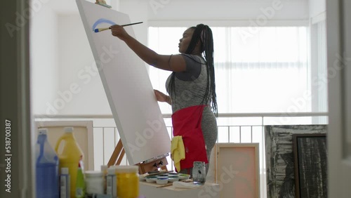 A young black female artist paints a beautiful canvas in her studio. 