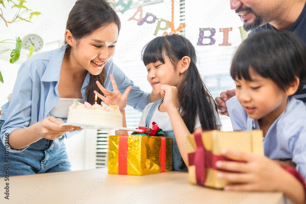 Asian family celebrating birthday together at home.Asian girl blow out candles on cake on table in happy birthday party and colors decorative items . Asian family celebrating birthday together at home.Asian girl blow out candles on cake on table in happy birthday party and colors decorative items .