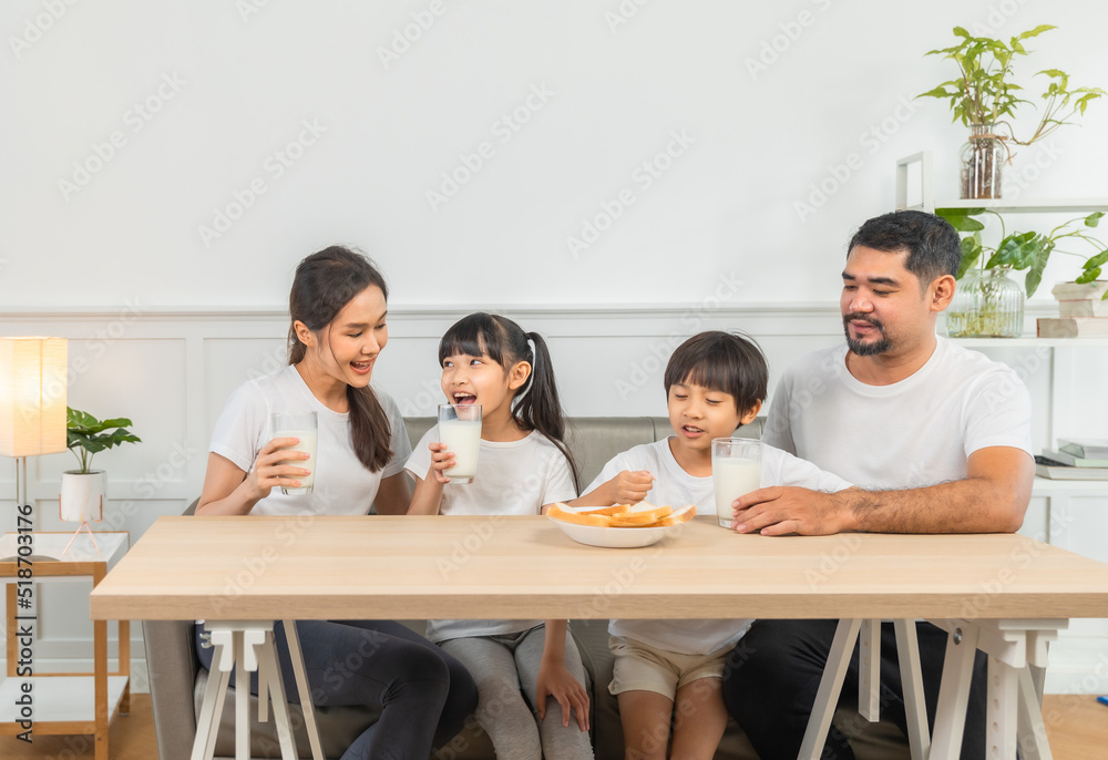 Asian family enjoying breakfast at living room. little girl daughter sitting on table, drinking milk with smiling father and mother in morning. Happy family at home. Asian family enjoying breakfast at living room. little girl daughter sitting on table, drinking milk with smiling father and mother in morning. Happy family at home.