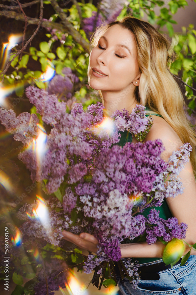 Fototapeta premium a beautiful woman in a green top and jeans with lilac flowers. solar flare.