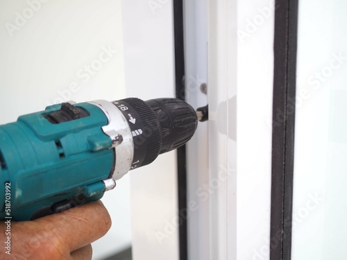 Asian man locksmith installing a lock on a new white door with a hand drill. closeup photo, blurred.