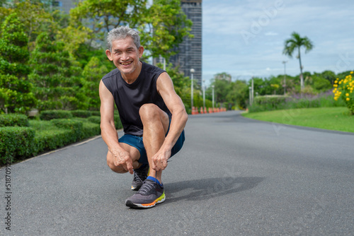 happy senior man with grey hair in sportswear tying shoe during running, a healthy elder people running in the city park. concept for elderly people health care, lifestyle, quality of life