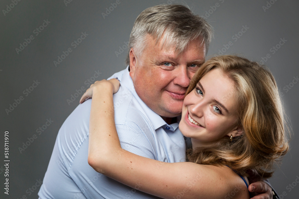 Dad and teenage daughter laugh and hug. A fat man in a shirt and a beautiful girl in a blue dress on a dark gray background. Love and tenderness. Close-up. Dad and teenage daughter laugh and hug. A fat man in a shirt and a beautiful girl in a blue dress on a dark gray background. Love and tenderness. Close-up.