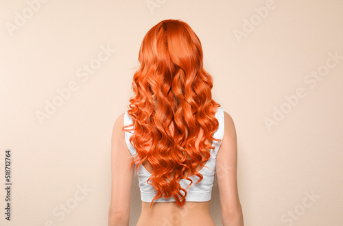 Beautiful woman with long orange hair on beige background, back view photo