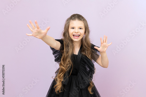 A happy little girl with wavy hair in a black dress on a pink isolated background. A beautiful child with a big smile.
