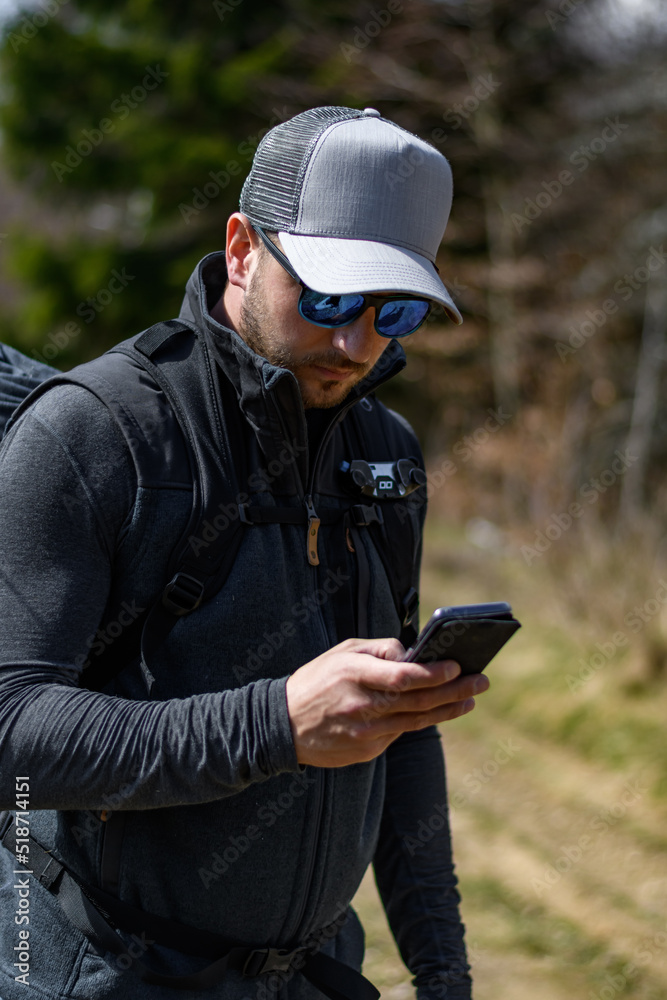 junger Mann mit Basecap schaut in der Natur auf sein Smartphone junger Mann mit Basecap schaut in der Natur auf sein Smartphone