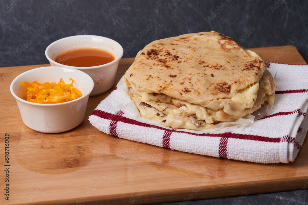 Pupusas on a wooden board with curtido and sauce over a black marble background Pupusas on a wooden board with curtido and sauce over a black marble background