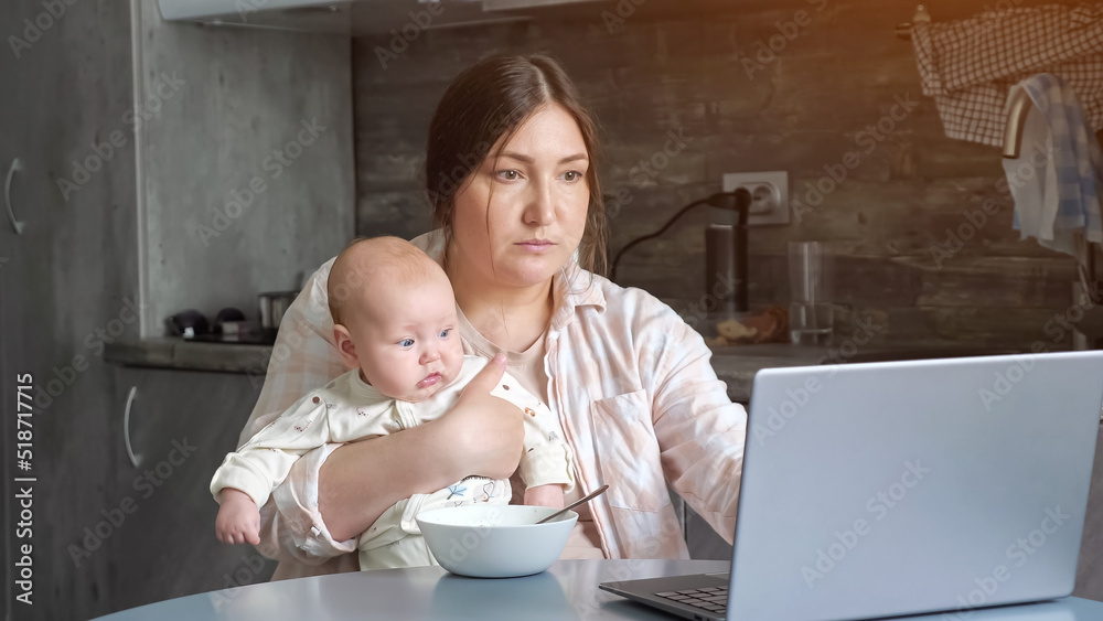 Mother eats porridge and works as freelancer with baby girl sitting in arms and watching around. Busy woman has lunch during working on laptop, sunlight Mother eats porridge and works as freelancer with baby girl sitting in arms and watching around. Busy woman has lunch during working on laptop, sunlight