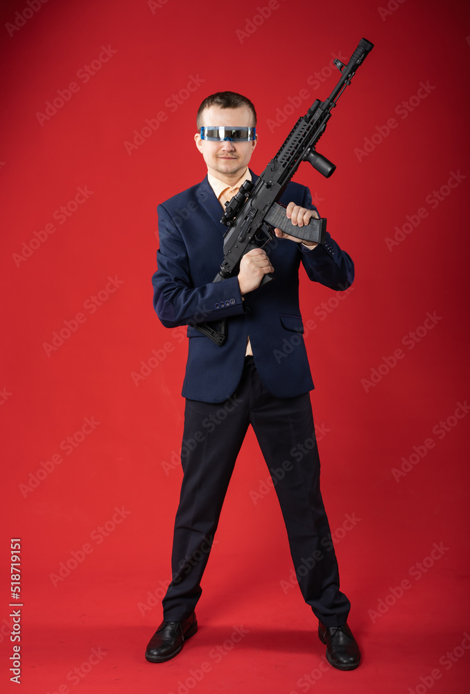 businessman with a gun. a guy in fashionable glasses, a suit holds a machine gun. Business concept. red background businessman with a gun. a guy in fashionable glasses, a suit holds a machine gun. Business concept. red background