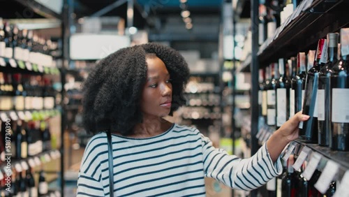 Wallpaper Mural Beautiful african american woman with dark curly hair standing at supermarket and choosing right wine among many other options on shelves. Grocery shopping. Torontodigital.ca