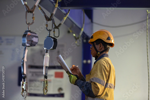 Authorise auditor personal wearing side impact safety helmet standing inspecting an inertial reel fall arrest, fall restraint equipment at training centre attached with structure beam prior used  photo