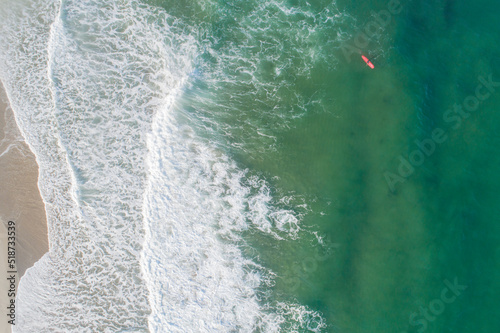 Aerial view of sandy beach and ocean with waves surfer waiting for the good wave