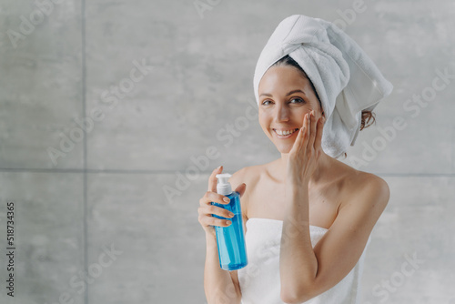 Face toner or micellar water. Gorgeous caucasian woman applying toner in flacon touching pure skin.