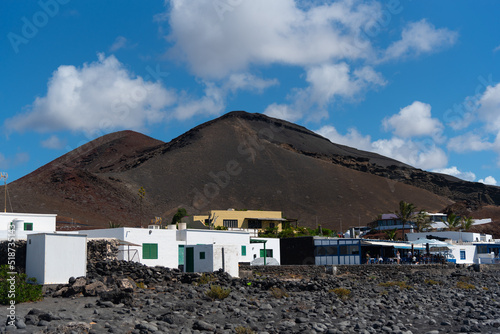 Village of traditional white houses with an inactivo volcano on black land in a volcanic environment in Lanzarote, Canary Islands, on a summer day with a clear blue sky. Natural tourist resources.