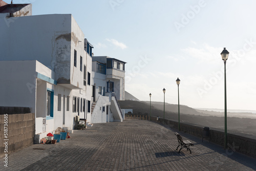 Pueblo La Santa en Lanzarote, vista de sus calles y casas con la tradicional arquitectura de las Islas canarias en color blanco junto al mar, al fondo grandes montañas volcánicas junto