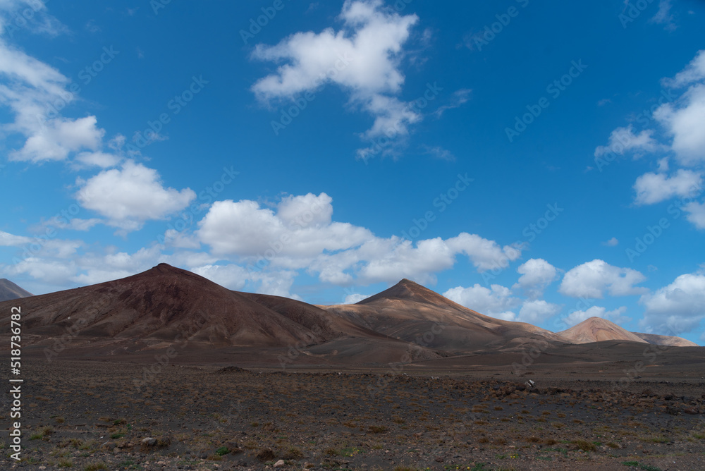 Vista panorámica del Parque Nacional de Timanfaya, un paisaje volcánico y desértico con grandes montañas en sombra durante un día soleado con el cielo azul y nubes en Lanzarote Islas Canarias. Vista panorámica del Parque Nacional de Timanfaya, un paisaje volcánico y desértico con grandes montañas en sombra durante un día soleado con el cielo azul y nubes en Lanzarote Islas Canarias.