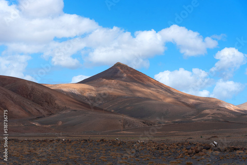 Vista panorámica del Parque Nacional de Timanfaya, un paisaje volcánico y desértico con una gran montaña iluminada durante un día soleado con el cielo azul y nubes en Lanzarote Islas Canarias.