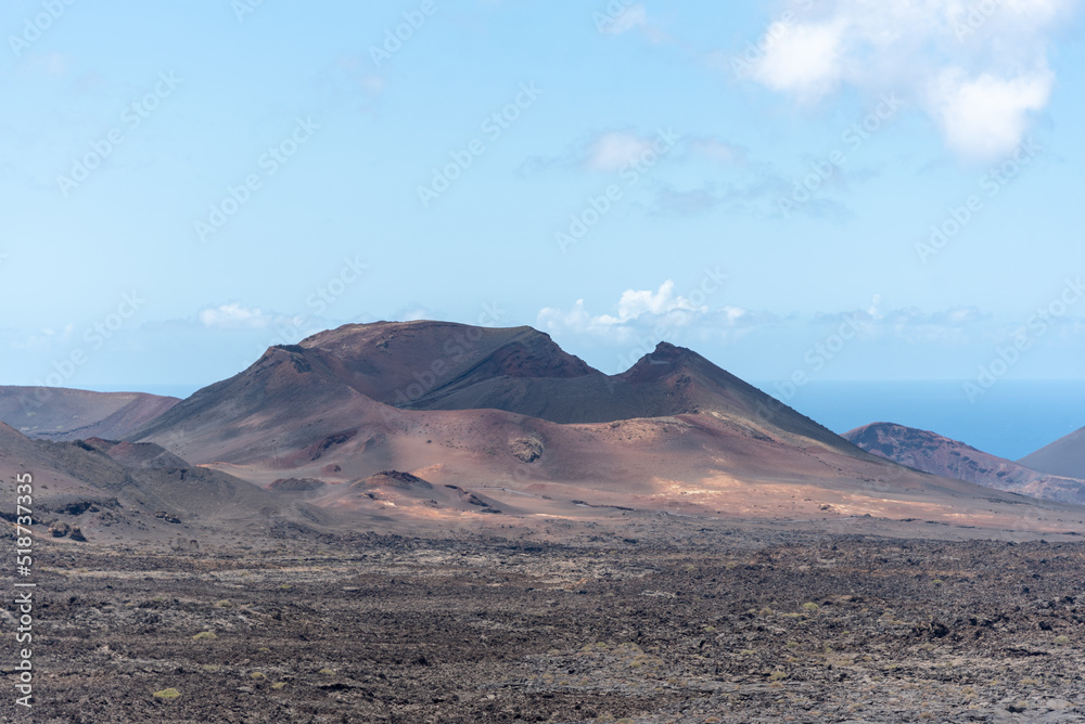 Vista panorámica de un paisaje volcánico y desértico con un gran volcán inactivo en medio y el mar al fondo en el Parque Nacional de Timanfaya en Lanzarote. Recursos naturales de las Islas Canarias.