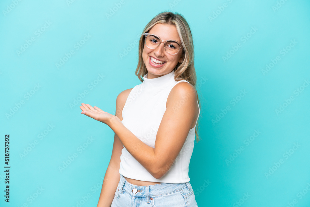 Young caucasian woman isolated on blue background presenting an idea while looking smiling towards Young caucasian woman isolated on blue background presenting an idea while looking smiling towards