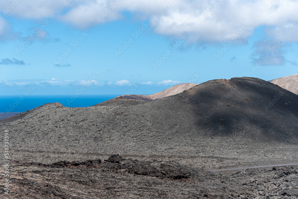 Φωτογραφία Paisaje desértico y volcánico con grandes volcanes inactivos  y el mar al fondo en el Parque Natural de Timanfaya en Lanzarote, Islas Canarias, durante un día soleado con el cielo azul despejado