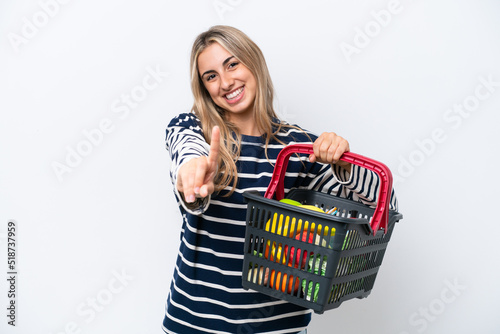 Young caucasian woman holding a shopping basket full of food isolated on white background showing and lifting a finger