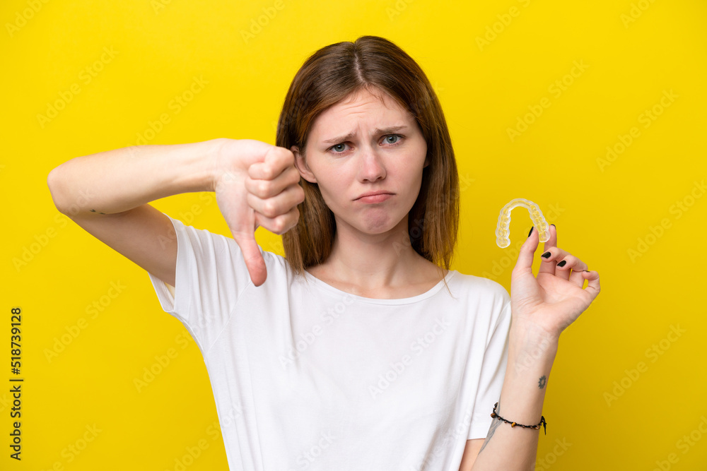 Young English woman holding invisible braces showing thumb down with negative expression Young English woman holding invisible braces showing thumb down with negative expression