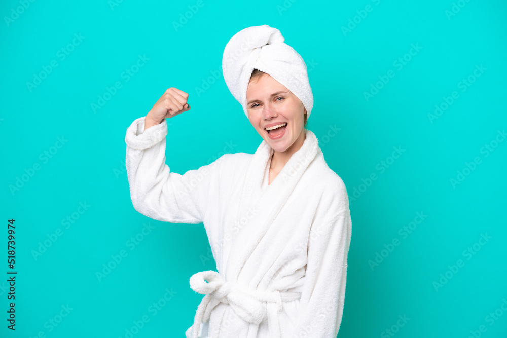 Young woman in a bathrobe isolated on blue background doing strong gesture