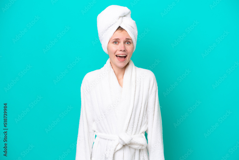 Young woman in a bathrobe isolated on blue background with surprise facial expression