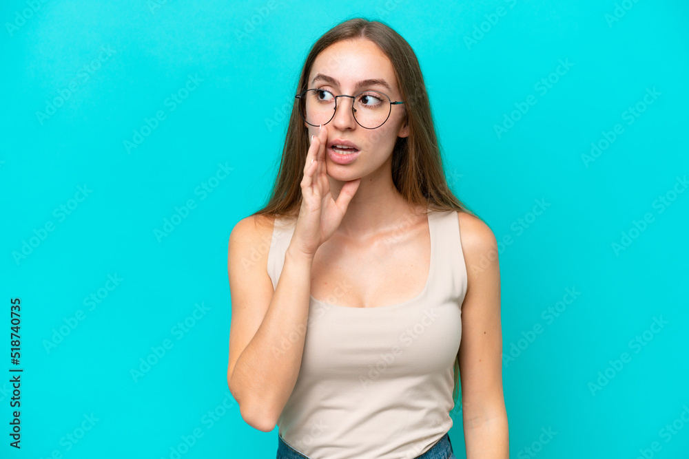 Young caucasian woman isolated on blue background whispering something with surprise gesture while looking to the side Young caucasian woman isolated on blue background whispering something with surprise gesture while looking to the side