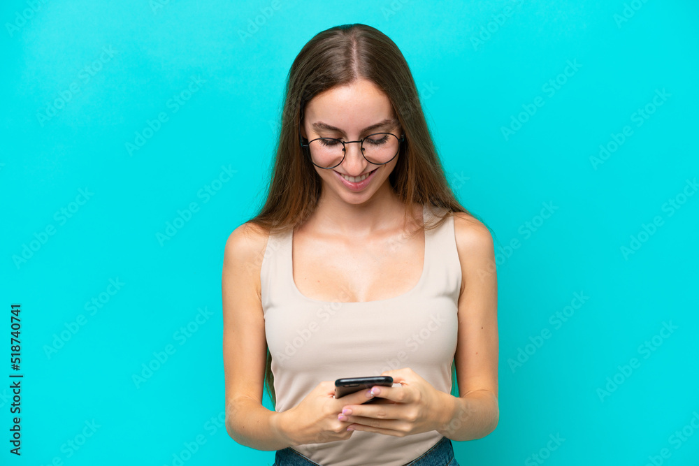 Young caucasian woman isolated on blue background sending a message with the mobile Young caucasian woman isolated on blue background sending a message with the mobile