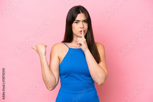 Young Brazilian woman isolated on pink background pointing to the side and doing silence gesture