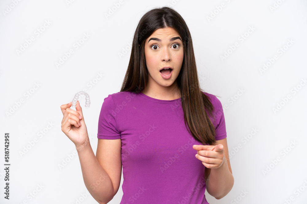 Young Brazilian woman holding invisible braces isolated on white background surprised and pointing front Young Brazilian woman holding invisible braces isolated on white background surprised and pointing front