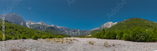 Hiking path on a dry riverbed leading from Valbona valley to Theth, a popular hiking spot in Albania leading through nice forests on a summerr day. Great panorama of Rrogam valley.