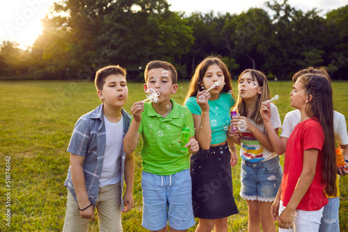 Little children enjoying holidays, playing in the park and having a great time together. Bunch of happy healthy kids standing on a green field on a warm summer day and blowing beautiful soap bubbles